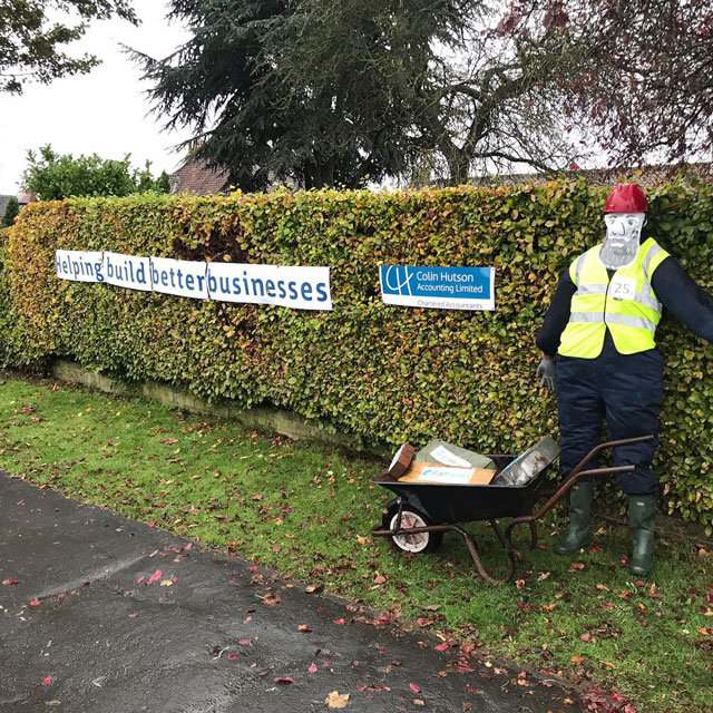 A scarecrow with a wheelbarrow, a sign behind it says 'Helping build better businesses; Colin Hutson Accounting Limited'